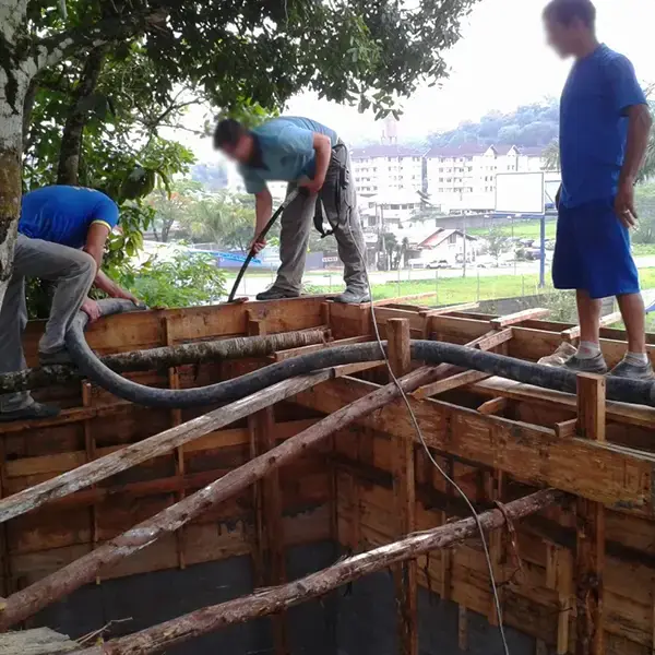Equipe conduzindo o mangote da bomba de concreto sobre as fôrmas do muro