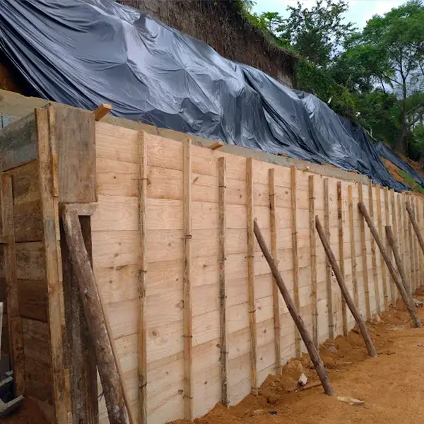 Fôrma de madeira escorada para a concretagem de um muro de contenção, com o talude coberto por lona