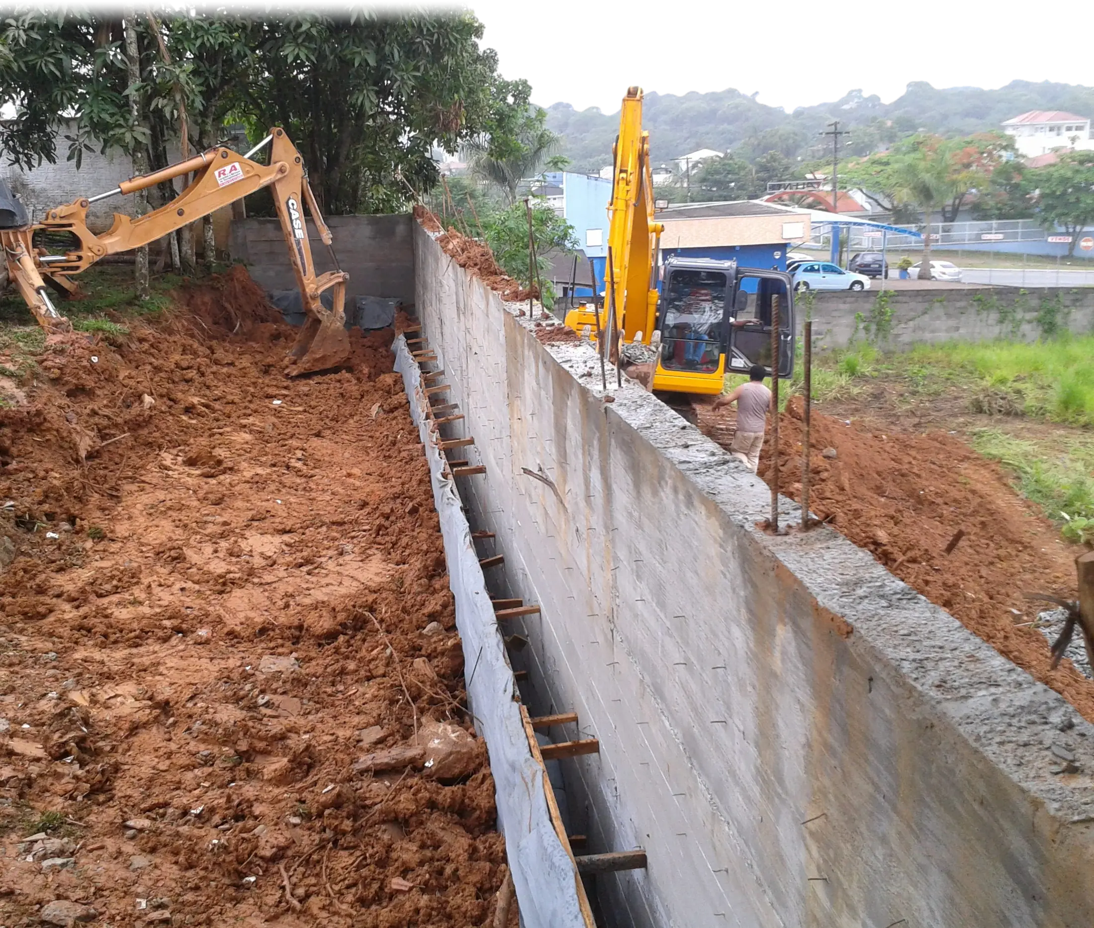 Muro de contenção em concreto armado recém-desformado, com escavadeiras na obra, em Joinville (SC)