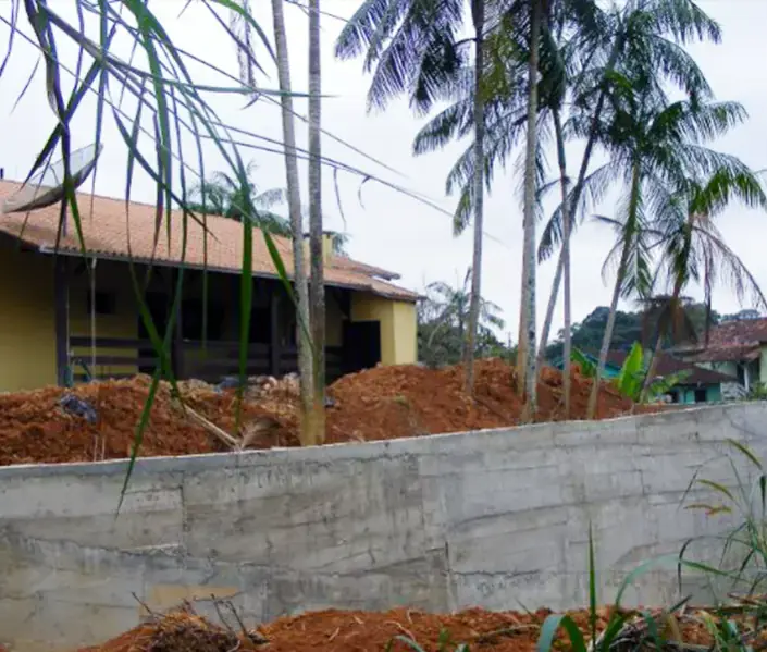 Muro de contenção em concreto armado no limite de um terreno, com uma casa ao fundo
