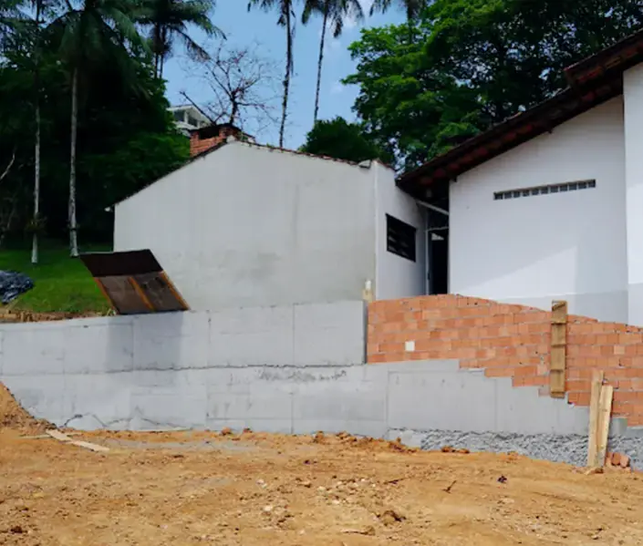 Muro de contenção em concreto armado ao lado de um galpão, com fechamento em blocos por cima